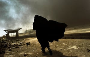An Iraqi woman walks through a plume of smoke rising from a massive fire at a liquid gas factory as she searches for her husband in Basra, Iraq, May 2003
