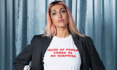 Camilla Mason with long straight pink hair and a white T-shirt saying 'abuse of power comes as no surprise'