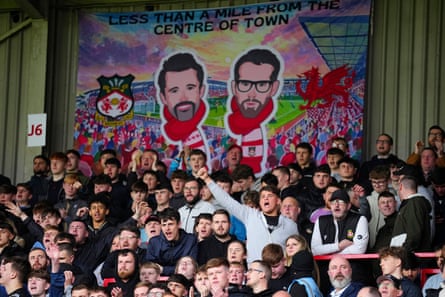 Wrexham supporters cheer successful nan stands pinch a banner depicting owners Ryan Reynolds and Rob McElhenney