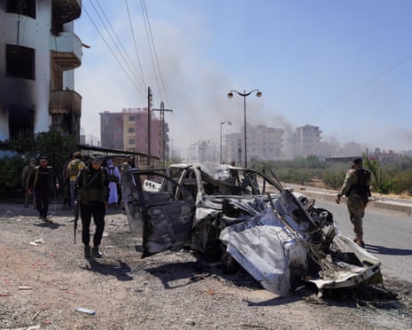 Bedouin fighters walk near a damaged car, following the Syrian presidency's announcement of a ceasefire after days of violence in Sweida province triggered by clashes between Bedouin fighters and Druze factions, in Sweida, Syria, July 19, 2025.