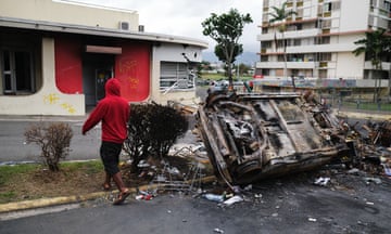 A man walks past a burnt vehicle in Magenta Tour district in Noumea, New Caledonia, earlier this week.