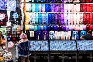 A woman with her back to the camera stands in front of a stall displaying soft toys and brightly coloured wigs