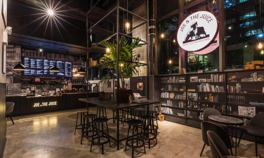 Interior of. acvafe with dark wood tones, high ceilings and a large circular pink illuminated signacing both in and out of the shop