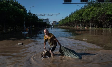 A man pulls a bag full of salvaged goods as he wades through flood waters in Zhuozhou, Hebei province, China, on Saturday