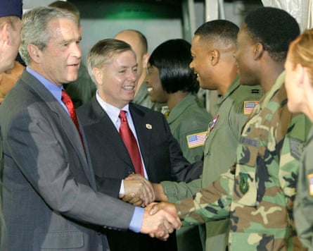 two men in suits shake hands with people in military uniforms