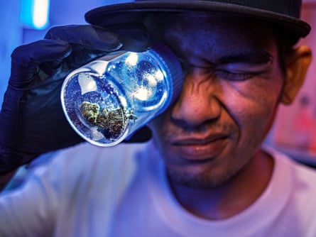 A seller holds a jar containing cannabis buds to his eye