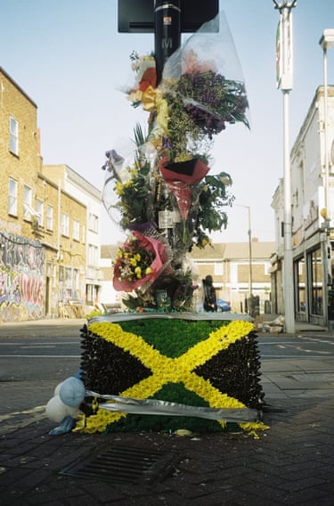 Colour photograph of bunches of flowers around a lamppost on top of a floral arrangement of the Jamaican flag.
