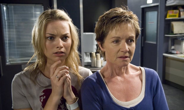 A young Donna stands with her hands clasped next to an older woman Susan, both looking at something offstage