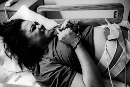 B/W photograph: handcuffed, pregnant inmate writhes in pain during a gynecological examination, moments before she gave birth by cesarean. Two armed guards were posted outside the open door to her hospital room.