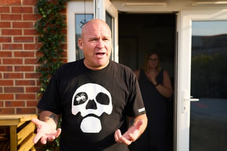 A man gesticulating outside his front door while his wife stands behind a fly screen in the doorway