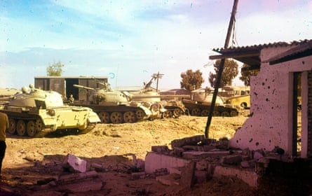 Blue and pink tinted photograph of tanks next to rubble from a destroyed building