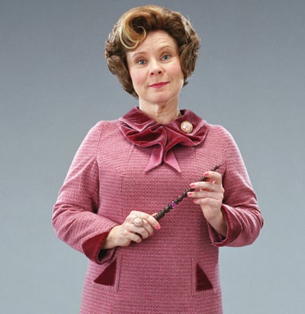 A woman in a dark pink coat with a velvet collar holding a wooden wand