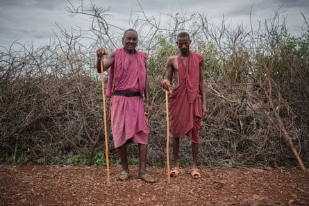 Two men with sticks pose for a photograph in front of some dry undergrowth