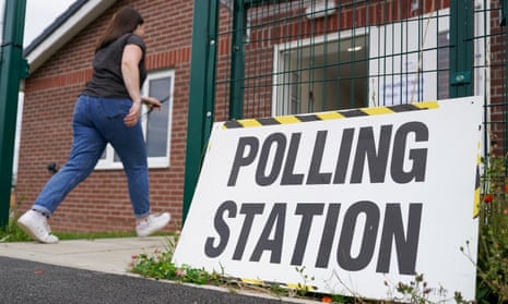 A polling station staff member enters a building following a sign that reads: 