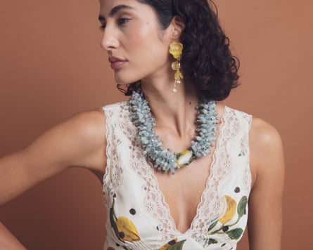 A woman wears a chunky blue beaded necklace and dangly, yellow, flower motif earrings