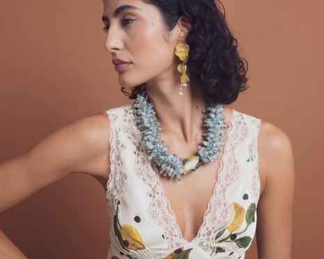 A woman wears a chunky blue beaded necklace and dangly, yellow, flower motif earrings