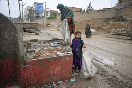 A man and a girl fill plastic bags with items picked from a large container with rubbish in it.