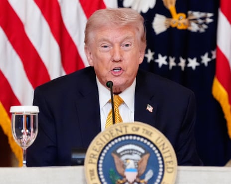 Donald Trump speaking into a microphone, American flags in the background