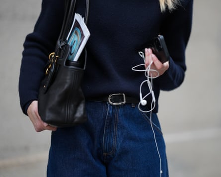Mirja Klein is seen wearing a navy fine knit turtleneck sweater with long sleeves and a fitted silhouette from COS; dark wash baggy jeans with a relaxed oversized barrel fit and rolled-up legs from Dark Park; a slim black leather belt with silver buckle; a black „Aventure“ nappa leather bag with gold hardware, chain link details and a belted detail in the front closure from Miu Miu; holding an iPhone smartphone and wearing white wired earphones on February 18, 2026 in Munich, Germany. (Photo by Moritz Scholz/Getty Images)