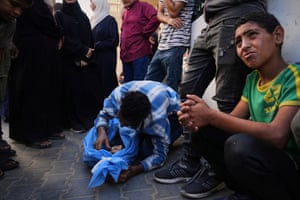 A boy in the foreground weeps as behind him a man crouches over a blue body bag with the face of girl just visible inside it