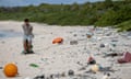 A man pulls a bag filled with rubbish along a white sand beach that has been destroyed by rubbish that washed up in the sea