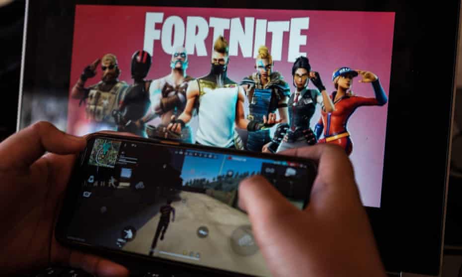 Picture of a child playing Fortnite on a phone, with a title screen for the game on a larger screen int he background.