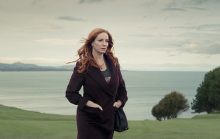 Christina Hendricks in a black suit, standing on a hill beside the water in Small Town, Big Story.
