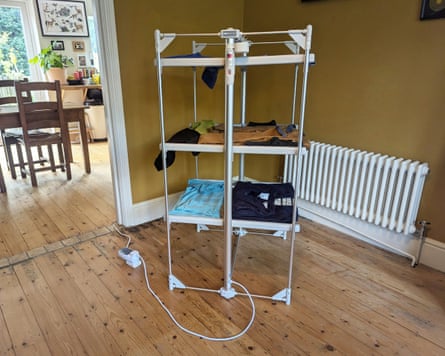 A heated, multi-tier clothes airer with hanging garments stands in a dining room near a radiator