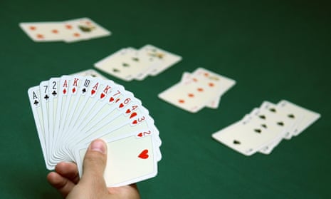Hand holding a deck of cards in front of a table with a green felt cloth and a bridge game set up