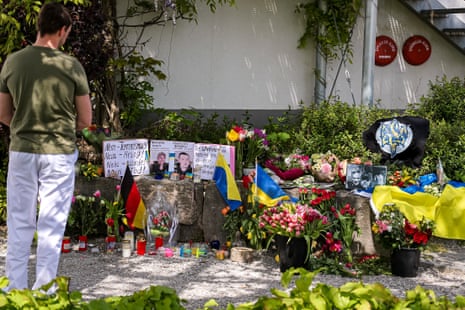 A man stands next to flowers and flags laid in front of a shopping center where two Ukrainian men have been stabbed to death, in Murnau, Germany, on Monday.