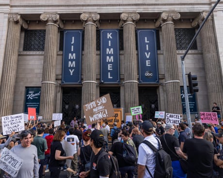a group of people stand outside building saying 'jimmy kimmel live' and hold signs such as 'jimmy said nothing wrong!' 'cancel disney' and 'don't give up speak up'