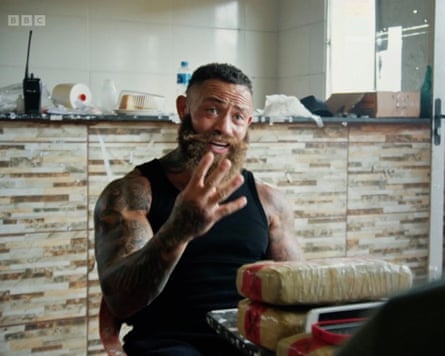 Ashley Cain in a black vest speaking to someone at a table and holding up four fingers.
