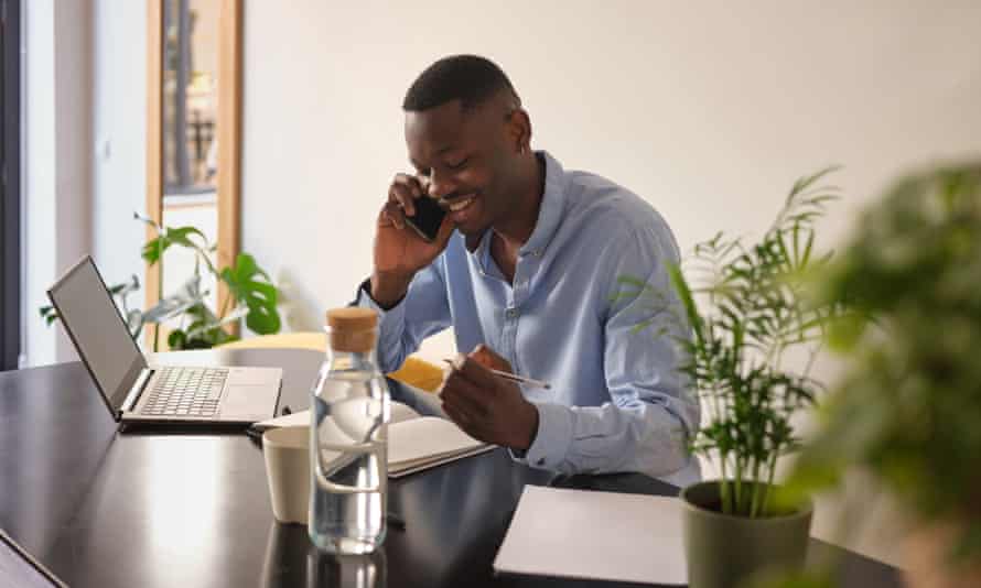 From boosting your mood to helping you focus: why water works wonders for your wellbeing 1 Smiling businessman in blue shirt talking on cell phone and arranging meeting, looking down in his planner while sitting at black desk in his office.