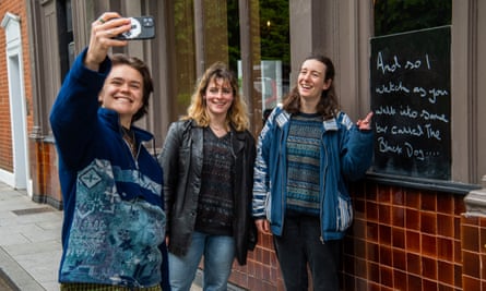 Three women pose for a selfie next to a blackboard bearing Taylor Swift lyrics outside the pub