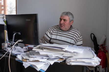 Marius Morozov sits at a desk looking at a computer screen, with papers piled on the desk in front of him