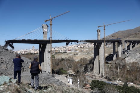 People on the ground look up at the bridge damaged by a strike.