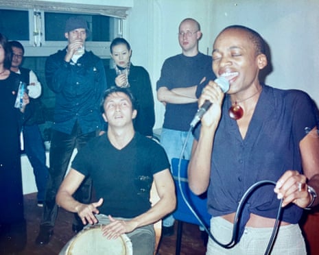 Camilla Balshaw singing into a mic next to a man playing a drum; a small group of people are watching the performance