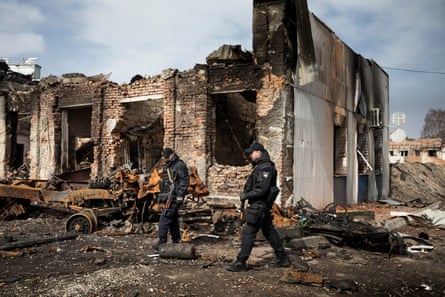 Police officers observe heavily damaged buildings in Trostianets