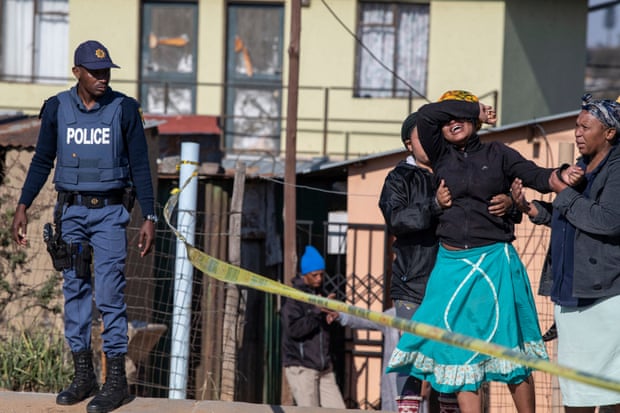 A relative of one of the victims is consoled as South African police officers refuse to let her cross the police barrier