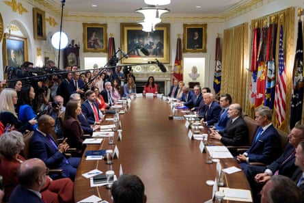 many people sit around a large table as media look on