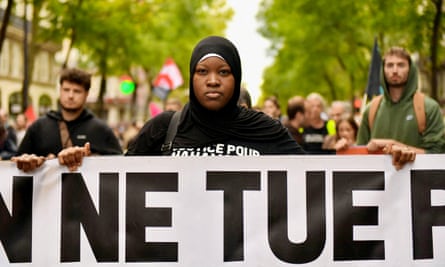 Black woman in headscarf with poster saying ‘Ne Tue Pas’ with crowds marching behind her