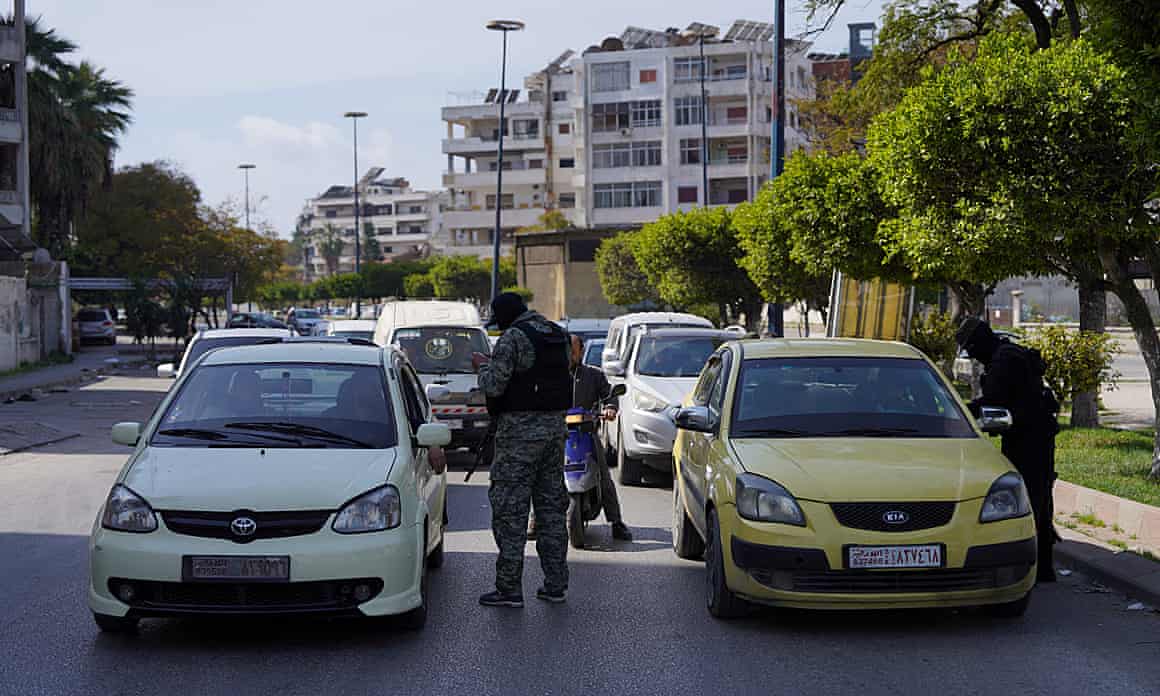 Members of Syrian security forces check cars in the city of Latakia=