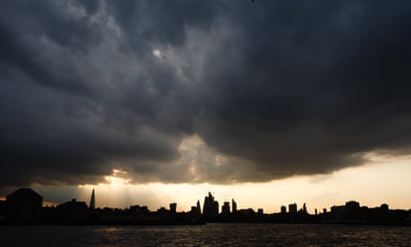 Dark clouds gather as the sun sets behind the towers of the City of London