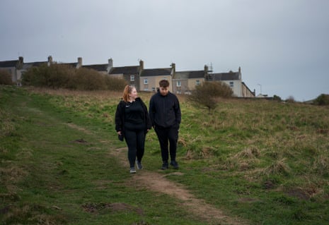 A girl and boy walk along a footpath near a row of terrace houses.
