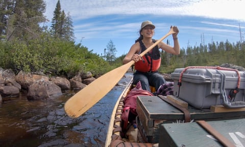 Woman paddling a canoe laden with stores down a river in the Canadian wilderness
