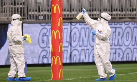 Cleaners in PPE sanitise the goal posts after an AFL match