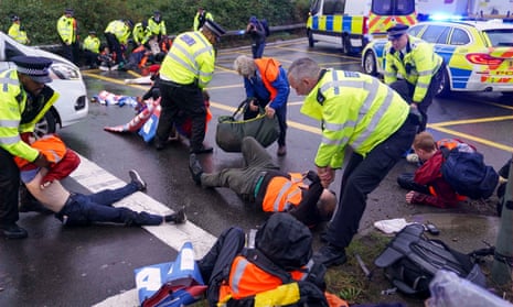 Police officers detain Insulate Britain activists occupying a roundabout leading from the M25 to Heathrow airport on 27 September.