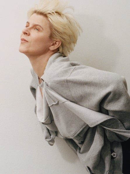 روبن مصورة من الخصر لأعلى، تميل إلى الإطار من الجهة اليمنى، مع يديها على وركيها، ترتدي سترة رمادية فاتحة مع وشاح مدمج