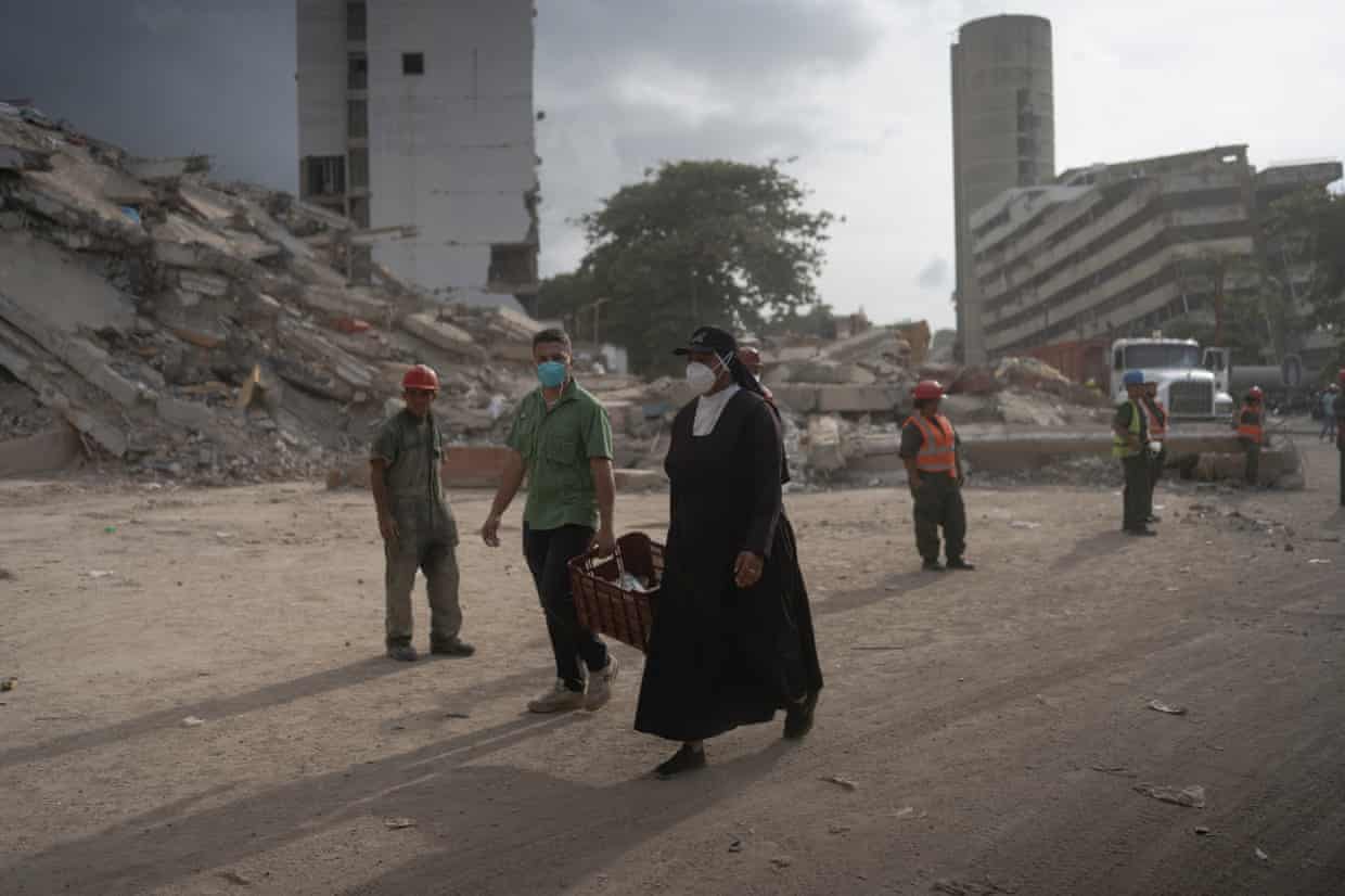 A nun walks in front of the wreckage of a building