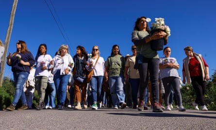 A line of women with arms linked walk behind another woman holding flowers